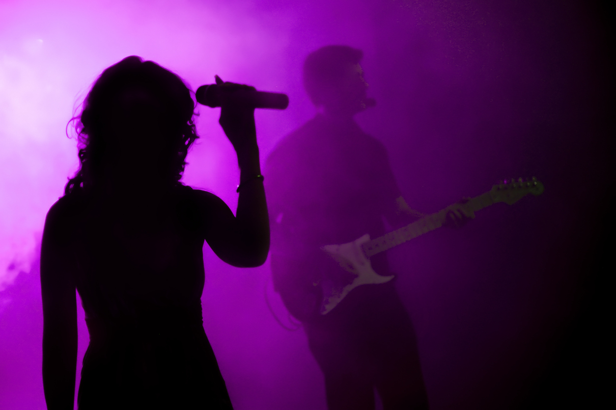 Silhouette of female holding microphone in purple light, representing the band Sonic Youth