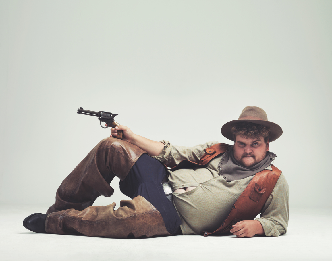 An overweight man dressed in a cowboy outfit in a sexy pose. He could be a desperado!